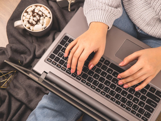 Woman typing on a laptop with hot cocoa to the side