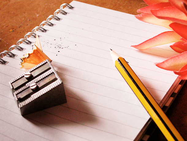 Photograph of a notebook with pencil, pencil sharpener, and a flower